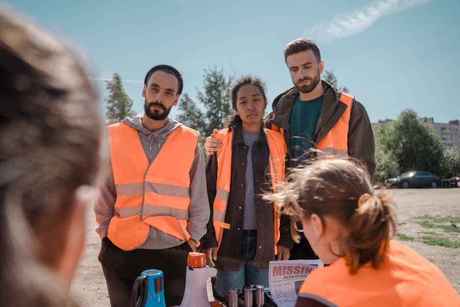 Group of volunteers wearing orange vests coordinating efforts outdoors on a sunny day.