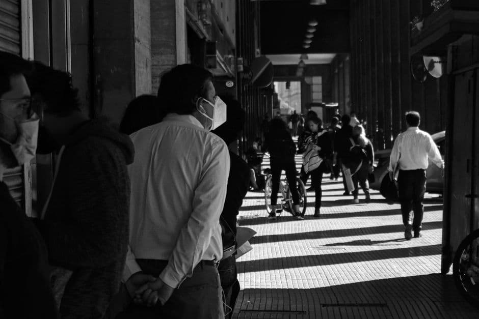People wearing masks walk through a busy Buenos Aires street in grayscale.