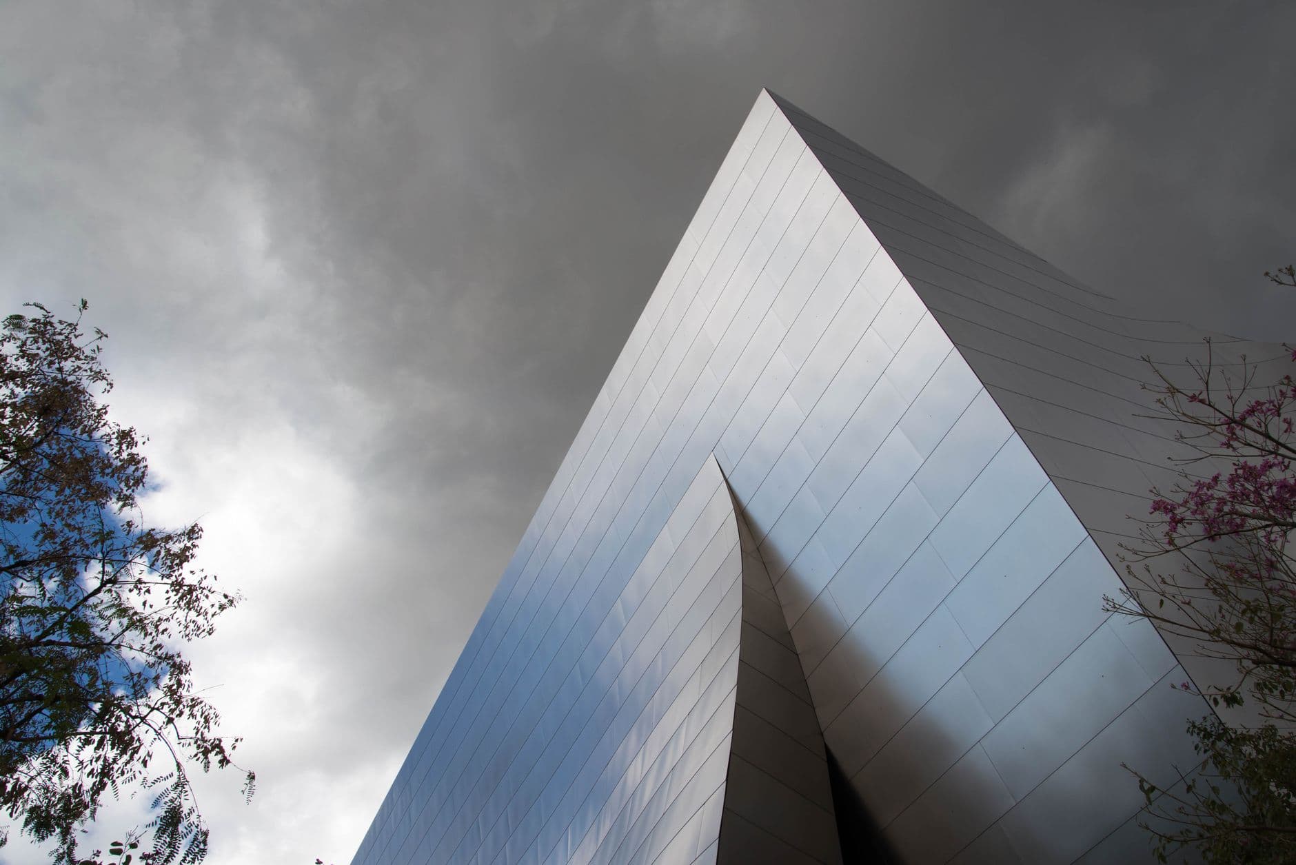 Modern architectural shot capturing a sleek, silver building with a dramatic cloudy backdrop.