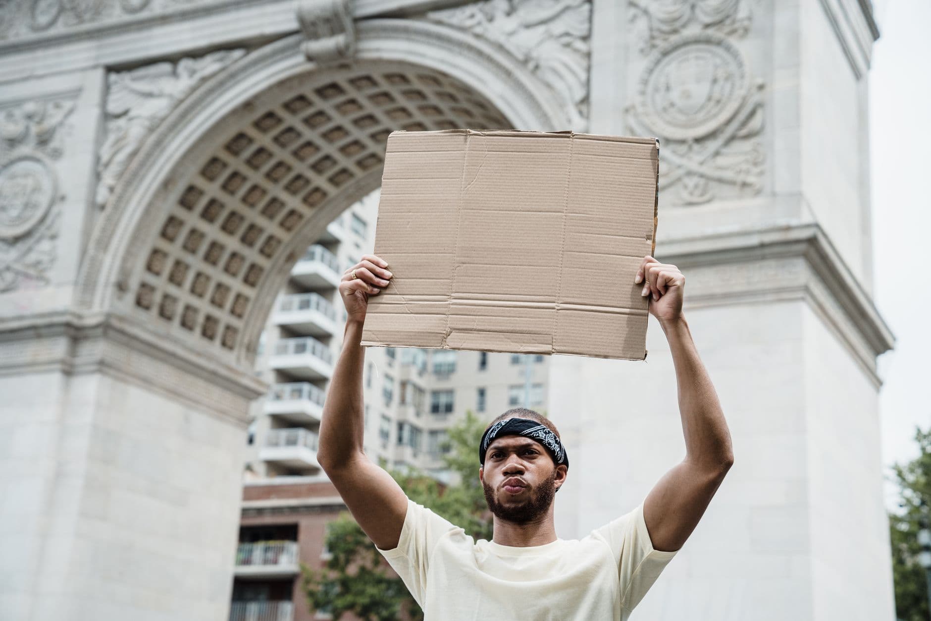 A man holds a blank cardboard sign near the Washington Square Arch, symbolizing activism and protest.